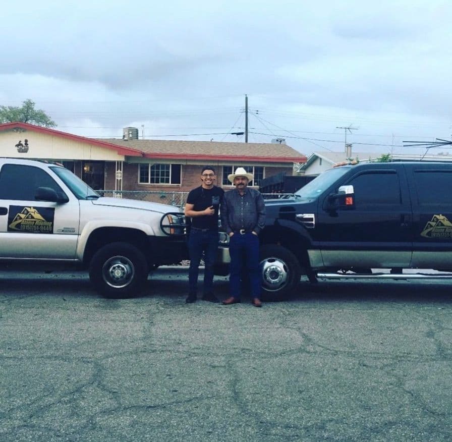 The owners of Alamo Roofing standing between two Alamo Roofing work trucks